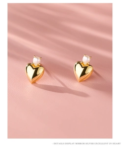 Detail of gold heart earrings with white pearls on a pink textured leather background