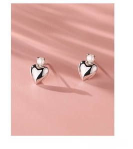 Detailed shot of S925 sterling silver heart earrings with white pearls on pink leather