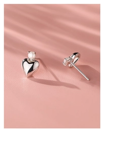 Detailed view of silver heart pearl studs with elegant shadow on pink background
