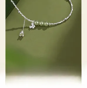 Close-up of silver butterfly lily of the valley bracelet with jade beads on green background