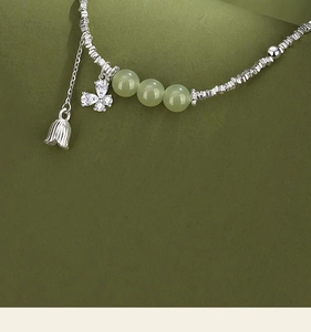 Macro detail of silver tulip bell and zircon butterfly charms on a jade bead bracelet
