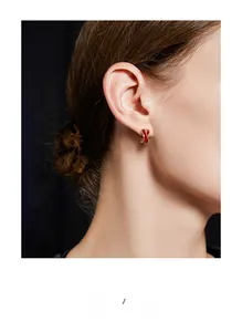 Close-up of a model wearing C-shaped red vintage earrings with gold trim on black background