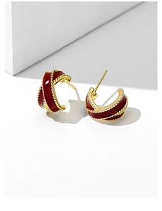 Close-up of vintage C-shaped gold-plated earrings with deep red enamel and beaded texture