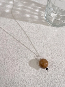 Detailansicht eines Saturn-Bernstein-Anhängers an einer feinen silbernen Pulloverkette