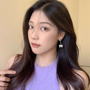 Détail de boucles d'oreilles pendantes avec cœur doré et nœud blanc portées par un modèle