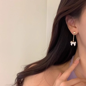 Vue détaillée de longues boucles d'oreilles cœur doré avec nœud blanc et perles