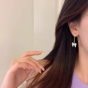 Vue détaillée de boucles d'oreilles longues cœur et nœud dorées portées par un mannequin