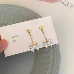 Détail de boucles d'oreilles cœur avec pendentif nœud en émail blanc et chaîne longue