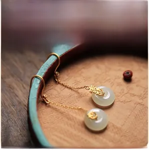 Gros plan de boucles d'oreilles Xi dorées avec disques de jade blanc et coffret bleu
