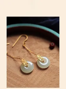 Vue macro de boucles d'oreilles en or avec signe Xi et jade blanc sur tissu vintage