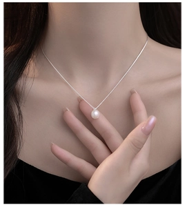 Detailopname van een minimalistische parelketting aan een fijne zilveren ketting bij model