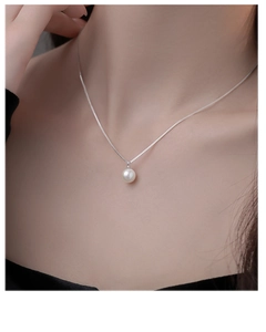 Detailopname van een minimalistische witte parelhanger aan een fijne zilveren boxketting
