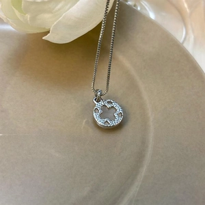 Detail of silver clover pendant with textured finish on a ceramic jewelry tray