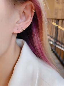 Close-up of golden snake-shaped ear cuffs and zircon stud earrings on model's ear