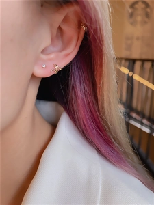 Detailed view of gold snake-style hoop earrings and zircon stud on a model's ear