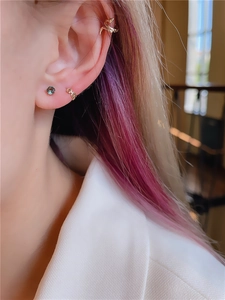 Close-up of golden snake ear cuff and blue gemstone stud for layered earring style