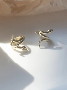 Detailed side view of snake-shaped gold earrings on a clean white textured surface