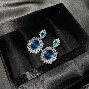 Vista detallada de pendientes de lujo con topacio azul ovalado y halo de diamantes