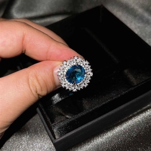 Primer plano de un anillo de lujo con topacio azul ovalado y doble halo de diamantes