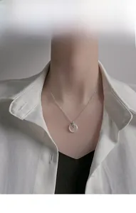 Detailed view of a silver necklace with a white circular pendant and green leaf design