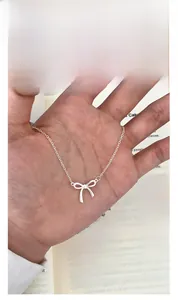 Silver bow pendant necklace detail held by hand over vintage book background