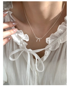 Close-up of a delicate silver bow pendant necklace worn by a model in a white blouse