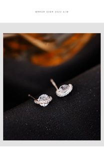 Close-up of silver planet stud earrings with white zircons on textured dark fabric