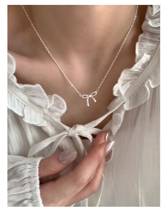 Close-up of elegant silver bow pendant necklace worn over a white ruffled shirt