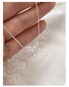 Detail of silver bow pendant necklace held by hand over white lace fabric background