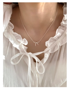 Close-up of a delicate silver bow pendant necklace worn by a model on a white blouse