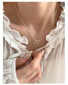Detail of elegant silver bow pendant necklace worn on a model with white lace shirt