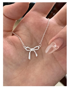 Close-up of a delicate silver bow pendant necklace held in hand to show the fine details