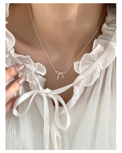 Close-up of a silver bow necklace pendant on a white ruffled shirt for a delicate look
