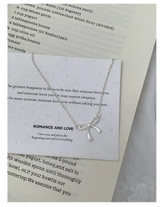 Elegant silver ribbon bow necklace displayed on a romantic white gift card with book background