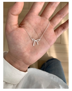 Close-up of a delicate silver bow pendant necklace held by hand for a detailed texture view