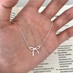 Elegant silver ribbon bow pendant necklace on a delicate chain held in hand