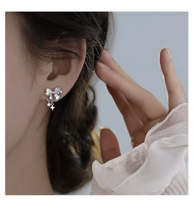 Detail of silver bow earrings with white zircons and star drop on model ear