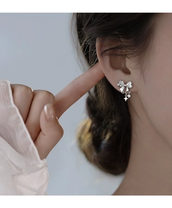 Detail of silver bow earrings with sparkling stones and dangling star pendants on ear
