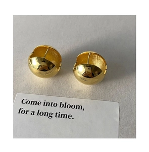 Détail de boucles d'oreilles boules dorées polies avec fermoir sur fond gris minimaliste