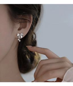 Close-up of silver bow earrings with zircon tassels on a model's ear