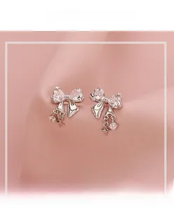 Close-up of silver bow earrings with zircon heart and star tassel on pink fabric