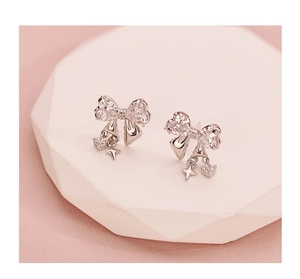Detail view of silver bow stud earrings with zircon stars and heart charms on silk