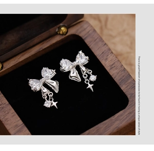 Macro shot of silver bow earrings with heart crystals and hanging star elements