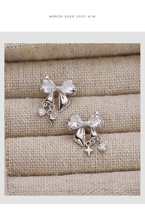 Detail view of silver bow earrings with heart cubic zirconia and star tassel charms