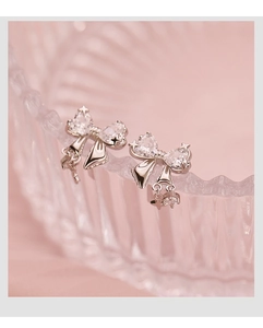 Detail of silver bow earrings with heart-shaped zircon and delicate metallic fringe