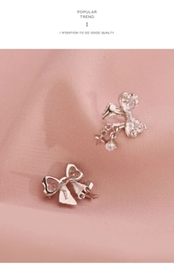 Detailed close-up of bow knot earrings with white zircons on soft pink fabric background