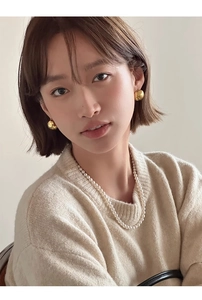 Gros plan de boucles d'oreilles boules dorées et collier de perles sur pull en maille