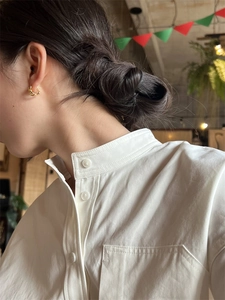 Détail des boucles d'oreilles créoles dorées torsadées portées avec une chemise blanche en coton