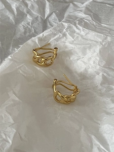 Gros plan de boucles d'oreilles chunky à maillons dorés sur fond de papier blanc minimaliste