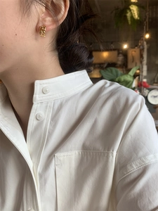 Gros plan de boucles d'oreilles chaînes dorées portées avec une chemise blanche à col montant